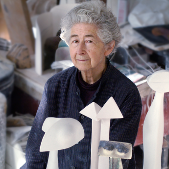 Ruth Duckworth sits in her studio surrounded by white and clear sculptures.