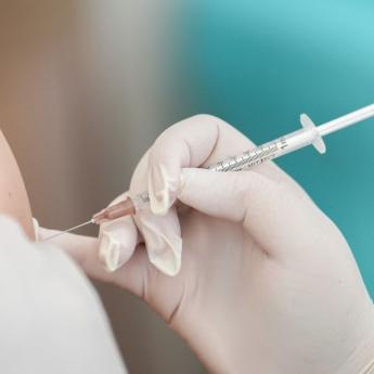 A medical professional wearing latex gloves administers a vaccine in a person's upper arm