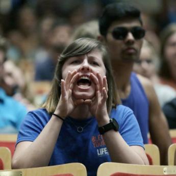 A woman in a blue shirt uses her hands to amplify her shout