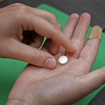 A person holds a white Mifepristone pill in their upturned right hand, while grabbing it with their left