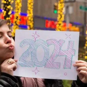 A woman blows a kiss to a sign with "2024" written in bubble letters