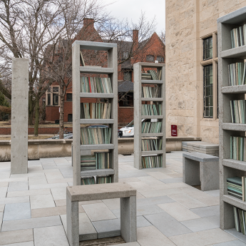 Several single bookcases filled with books made of a durable material dot the patio of the Neubauer Collegium.