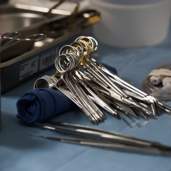 Several pairs of surgical scissors lay on top of one another amidst other medical supplies on a blue foundation