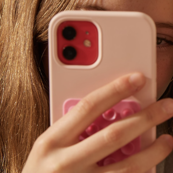 A girl holds up an iPhone with a pink case as though taking a photo of the viewer
