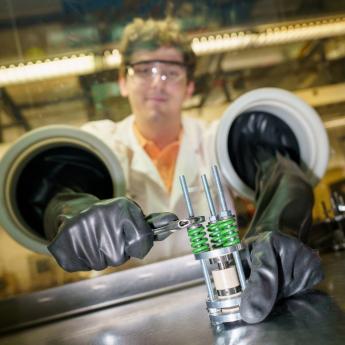 Photo of scientist with lab coat and glasses reaching into a glovebox