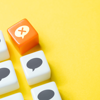 Rows of small white tiles with speech bubble sit on a yellow background. The right upper corner tile is orange with a speech bubble that contains an "X".