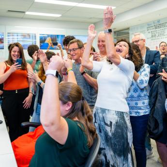 a room of scientists cheer in front of a bank of computers