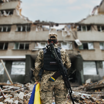 Ukrainian military woman with the Ukrainian flag in her hands on the background of an exploded house