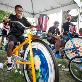 Two kids race stationary bikes at the Physics tent