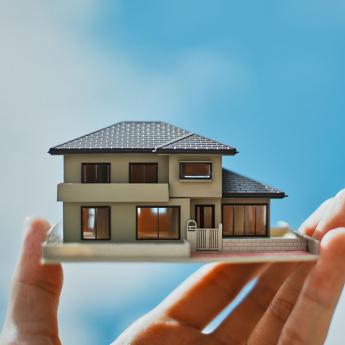 A hand holds a miniature model of a home