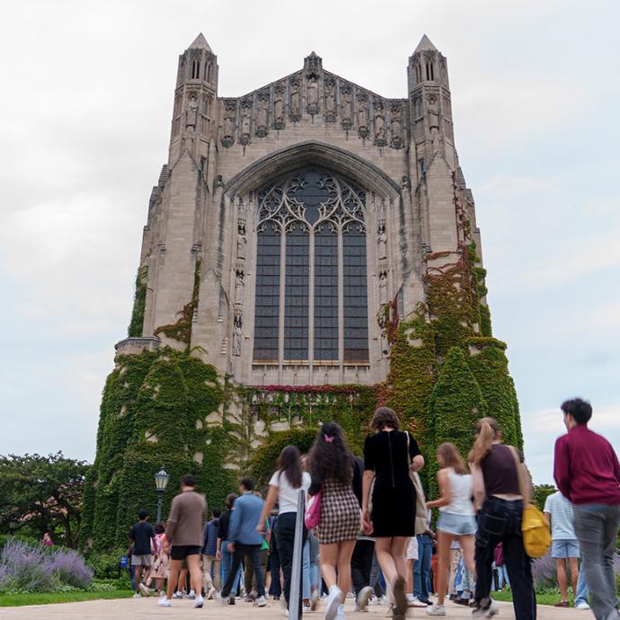 Photo of a large gothic-style cathedral with students walking up the steps on a sunny day
