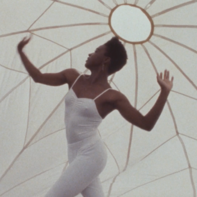 A dancer in a white bodysuit dances inside a white parachute.