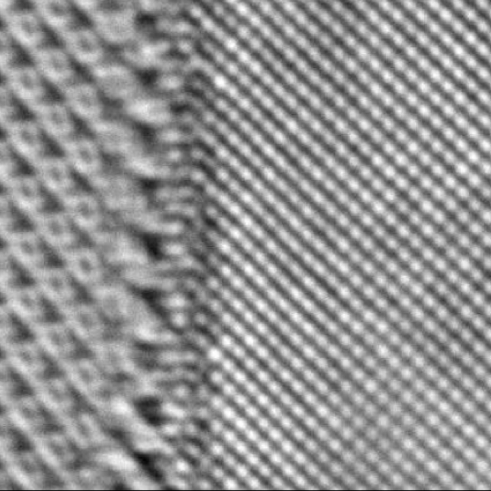 Black and white microscope image of two repeating lattices of atoms with a seam in the middle