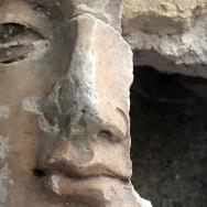 close-up on the face of a cracked plaster statue of a Buddha, with part of its cheek missing