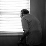 Elderly man standing with cane looking out window