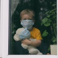 Child looking out window while hugging a stuffed animal