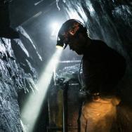 A coal miner with a headlamp works in a dark shaft
