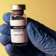 COVID-19 vaccine vial held by a hand in blue rubber gloves