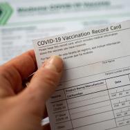 A person holds a COVID-19 vaccine card above an out-of-focus document