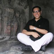 Art historian Wu Hung sits and smiles next to art carved into a wall