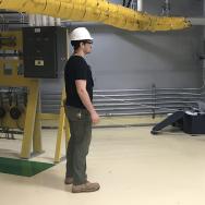 Man in hard hat stands near roped-off area with chest-height box in industrial setting