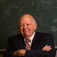 Prof. Emeritus Don York stands in front of a chalkboard with arms folded