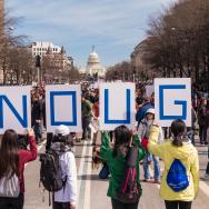 Six teens hold up signs in front of the US Capitol that spell ENOUGH