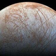 view of one hemisphere of Europa, a moon made of pale rock with orange streaks across surface