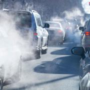 A group of cars sitting in traffic surrounded by clouds of vehicle exhaust