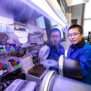 Prof. Sihong Wang in a lab coat standing in lab with hands in a glove box, looking at camera