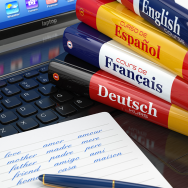 A stack of German, French, Spanish and English language books sits on a laptop keyboard next to a notebook and pen. Written on the notebook are translations for "love," "mother," "father," "family" and "home" in several languages.