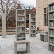 Several single bookcases filled with books made of a durable material dot the patio of the Neubauer Collegium.