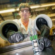 Photo of scientist with lab coat and glasses reaching into a glovebox