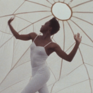 A dancer in a white bodysuit dances inside a white parachute.