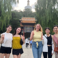 A group of five students on a bridge in front of a pagoda-like building and willow trees.