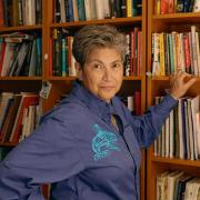 Photo of person standing at a wall of books and looking at camera