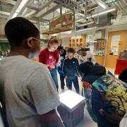 Photo of kids leaning around a glowing table in a lab.
